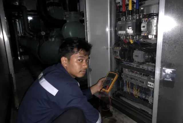 Teknisi memperbaiki panel chiller pada panggilan darurat malam hari
